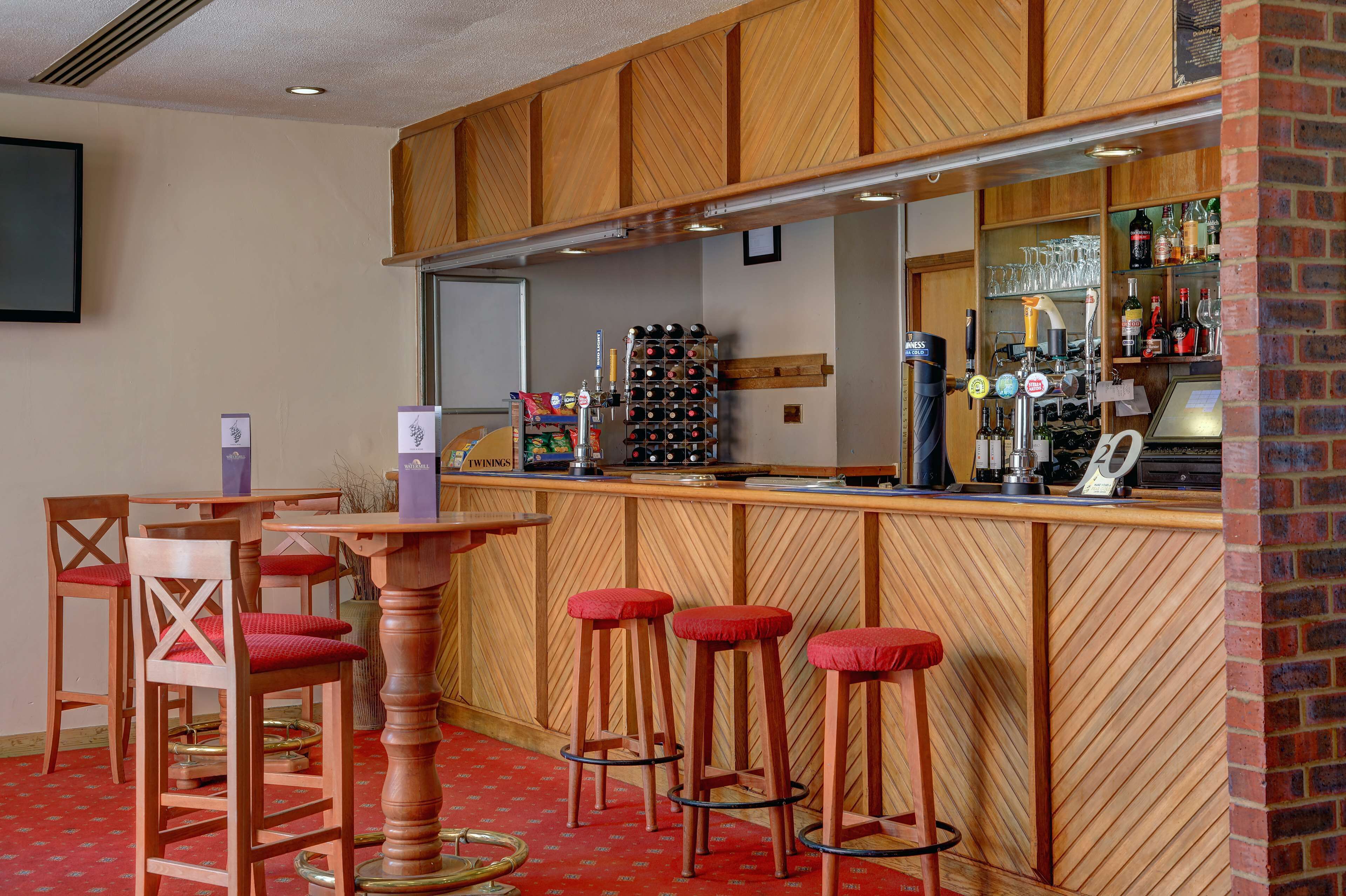 Zona de bar con taburetes de madera, una barra con botelleros y un área de asientos con sillas.