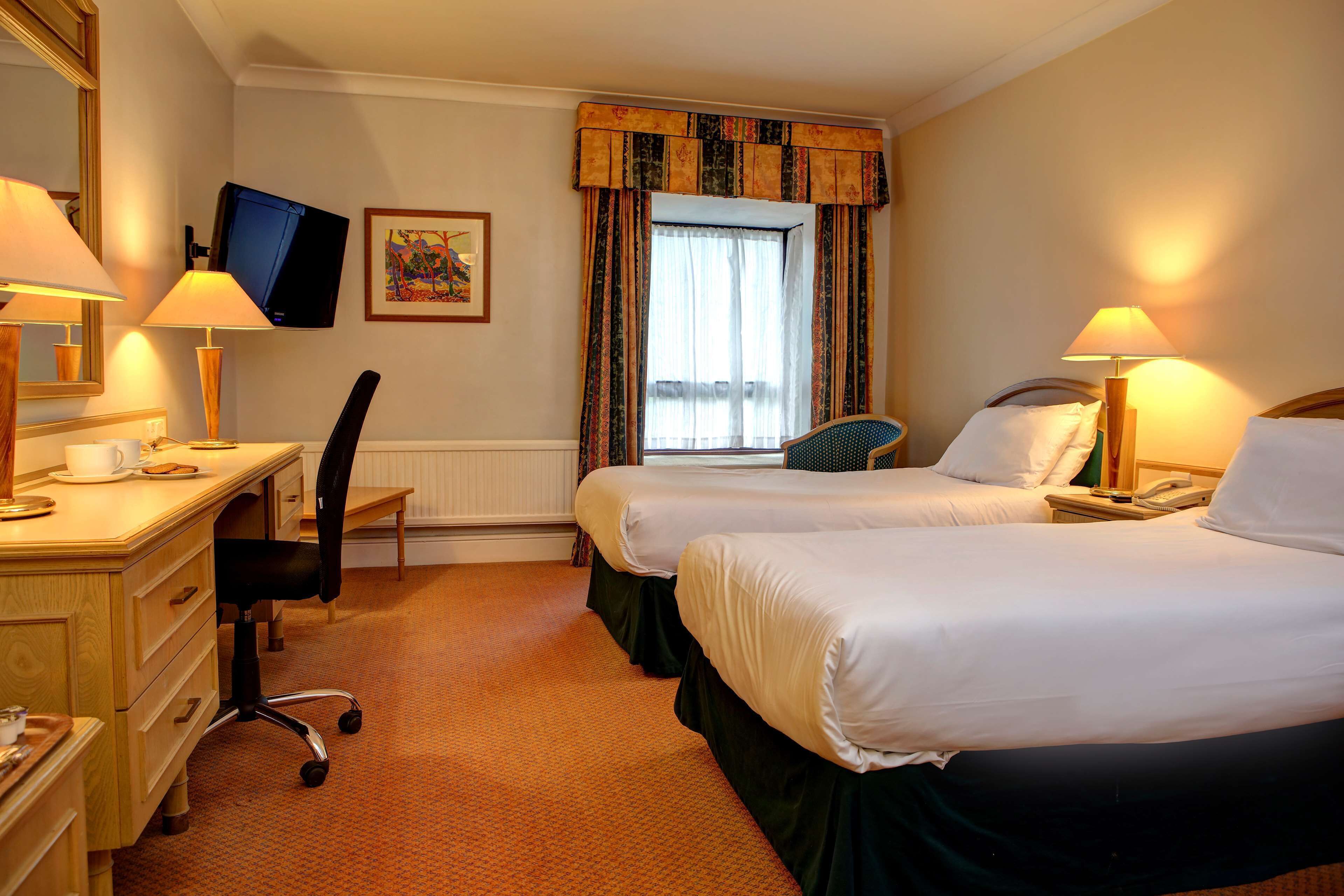 A hotel room with two beds, a desk with a chair, a television, and a window with curtains.