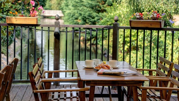 Terraza de madera con una mesa preparada para dos, con vista a un cuerpo de agua.