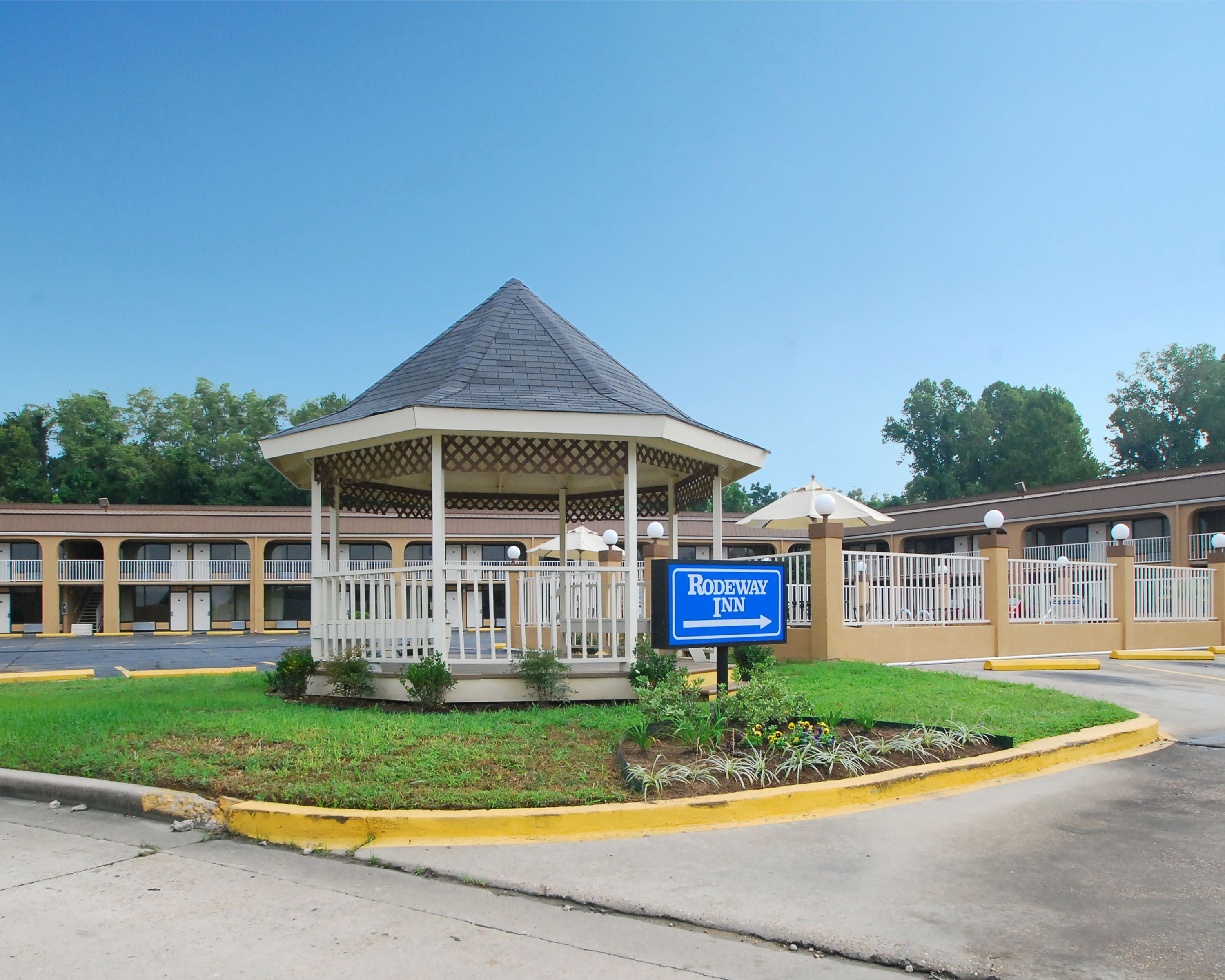 Um motel com um gazebo, uma placa da Rodeway Inn e um estacionamento.