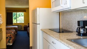 A compact hotel room with a kitchenette, a bed with a patterned bedspread, a window with curtains, and a view of greenery outside. - Rodeway Inn Vicksburg (Vicksburg)