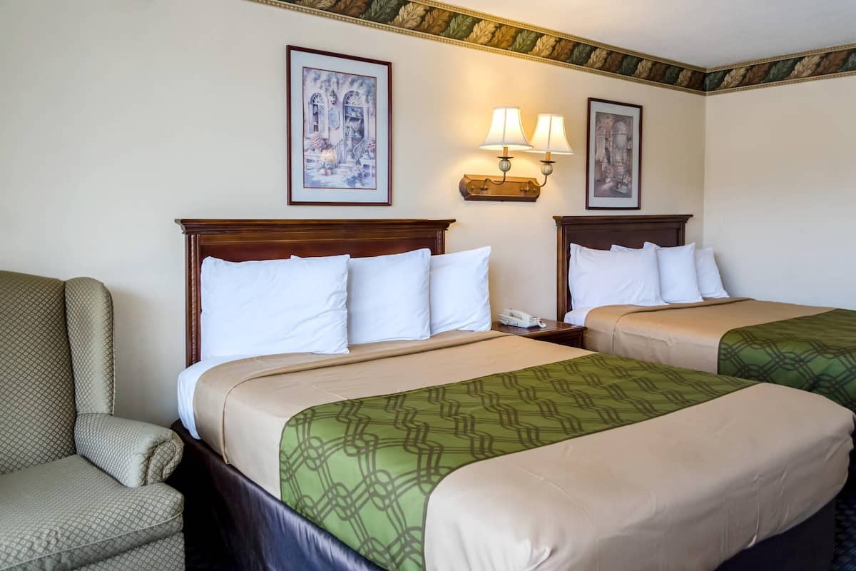 A hotel room with two beds, a chair, and a nightstand with a phone.