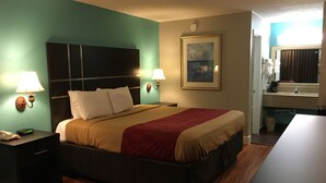 A hotel room with a bed, bedside lamps, a painting, a nightstand with a phone, and a small table. - Rodeway Inn Vicksburg (Vicksburg)