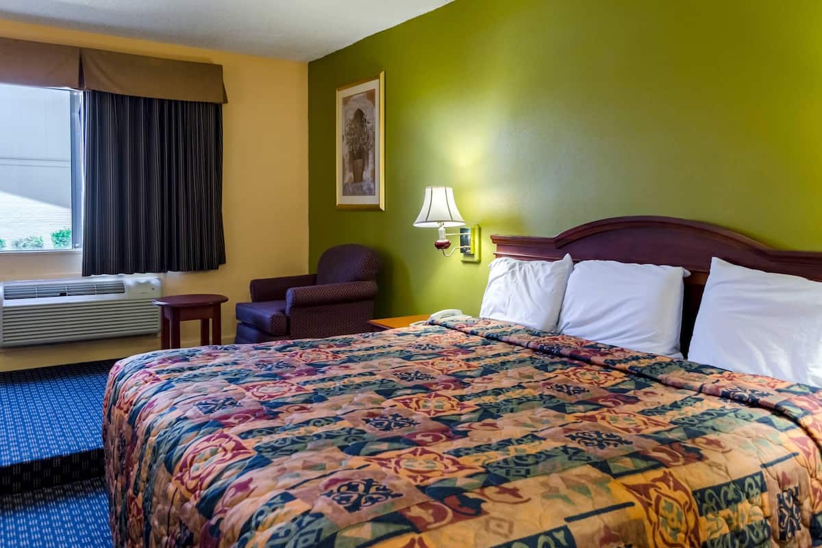 A hotel room with a large bed, a chair, a lamp, and a window with curtains.