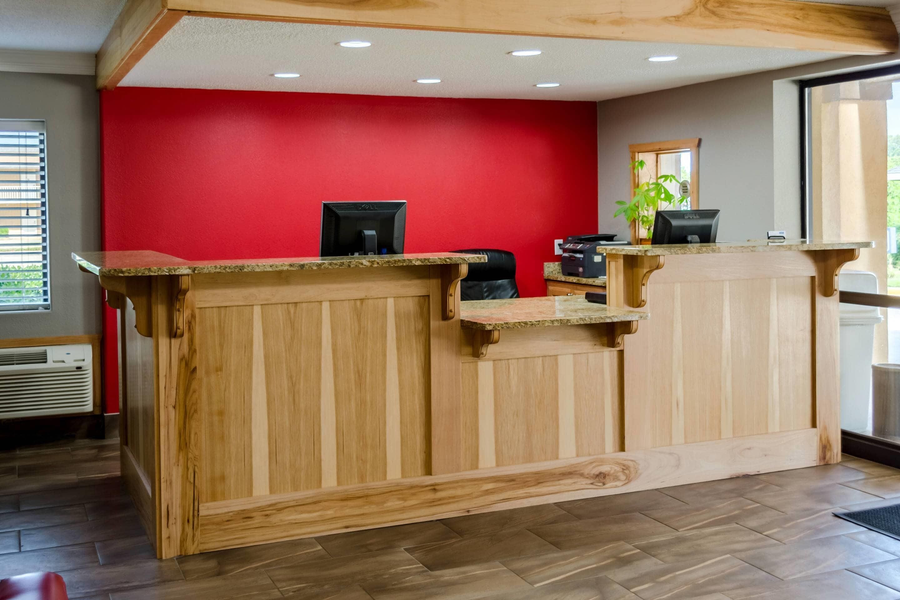 A reception desk with a red wall, wooden paneling, and a computer.