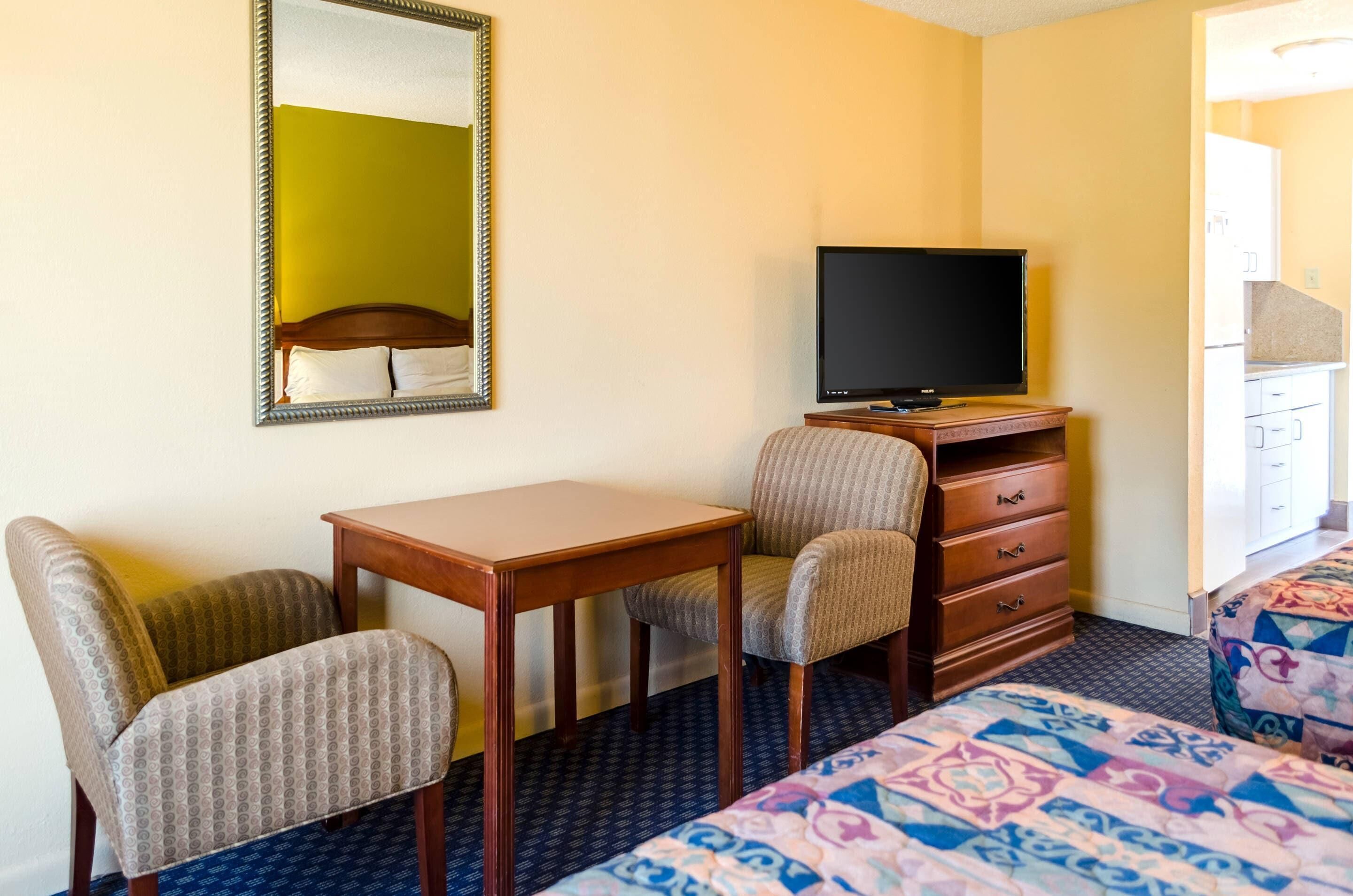 A hotel room with a bed, a desk, a chair, a television, and a dresser.