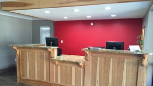 A reception desk with two computer monitors, a plant, and a red wall. - Rodeway Inn Vicksburg (Vicksburg)