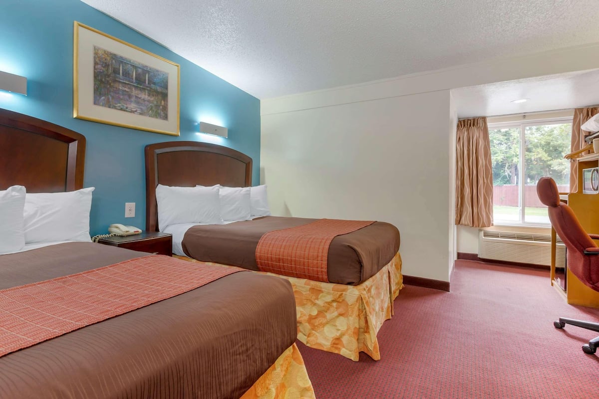 Une chambre d’hôtel avec deux lits, un tableau au mur, une fenêtre avec des rideaux et un bureau avec une chaise.
