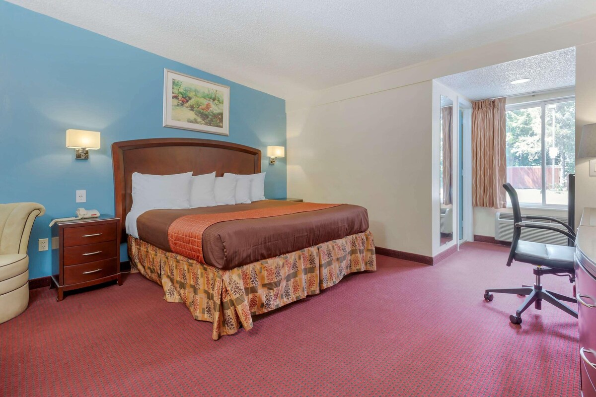 A hotel room with a bed, bedside tables, a chair, and a window.
