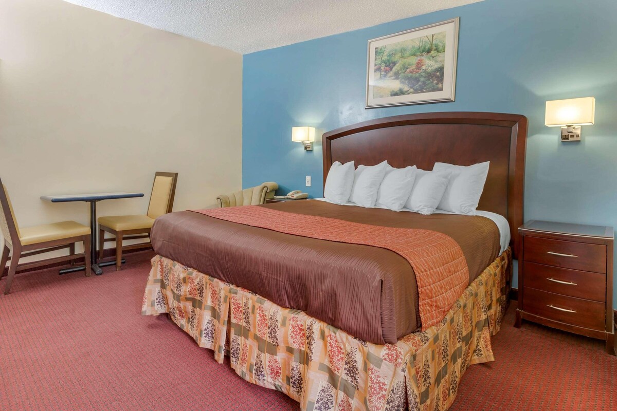 A hotel room with a bed, a desk, a chair, a nightstand, and two wall-mounted lamps.