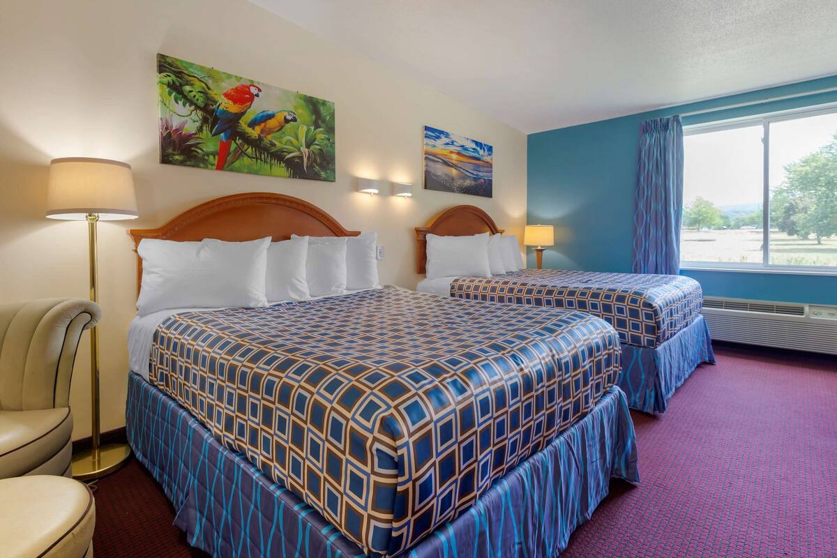Une chambre d’hôtel avec deux lits, un bureau, une chaise et une grande fenêtre donnant sur un beau paysage.
