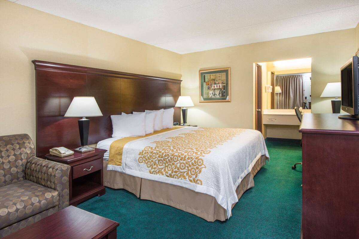 Een hotelkamer met een groot bed, twee nachtkastjes met lampen, een stoel, een bureau en een televisie.