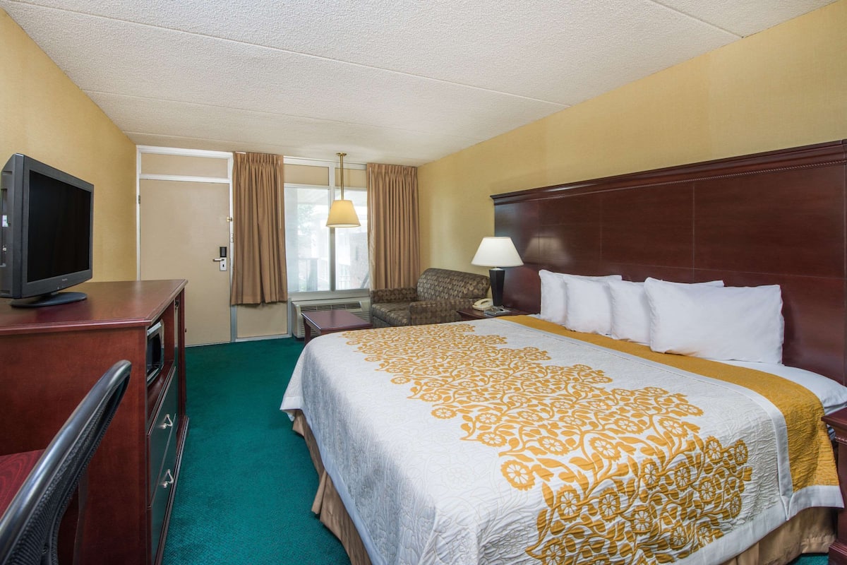 Een hotelkamer met een bed, een televisie op een bureau, een stoel, een lamp en een raam met gordijnen.