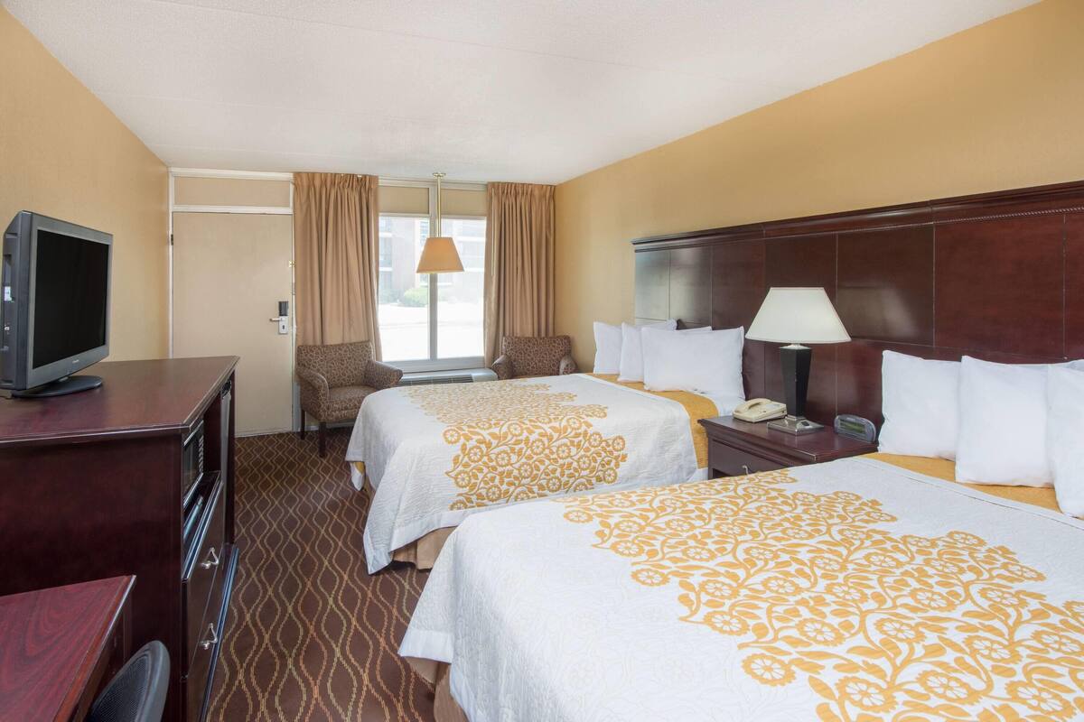 Een hotelkamer met twee bedden, een bureau met een televisie, een stoel, een lamp en een telefoon.