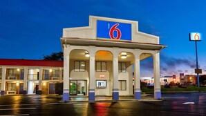 Un motel reconnaissable à son grand panneau indiquant le chiffre « 6 », à son toit rouge et à son entrée bien éclairée.