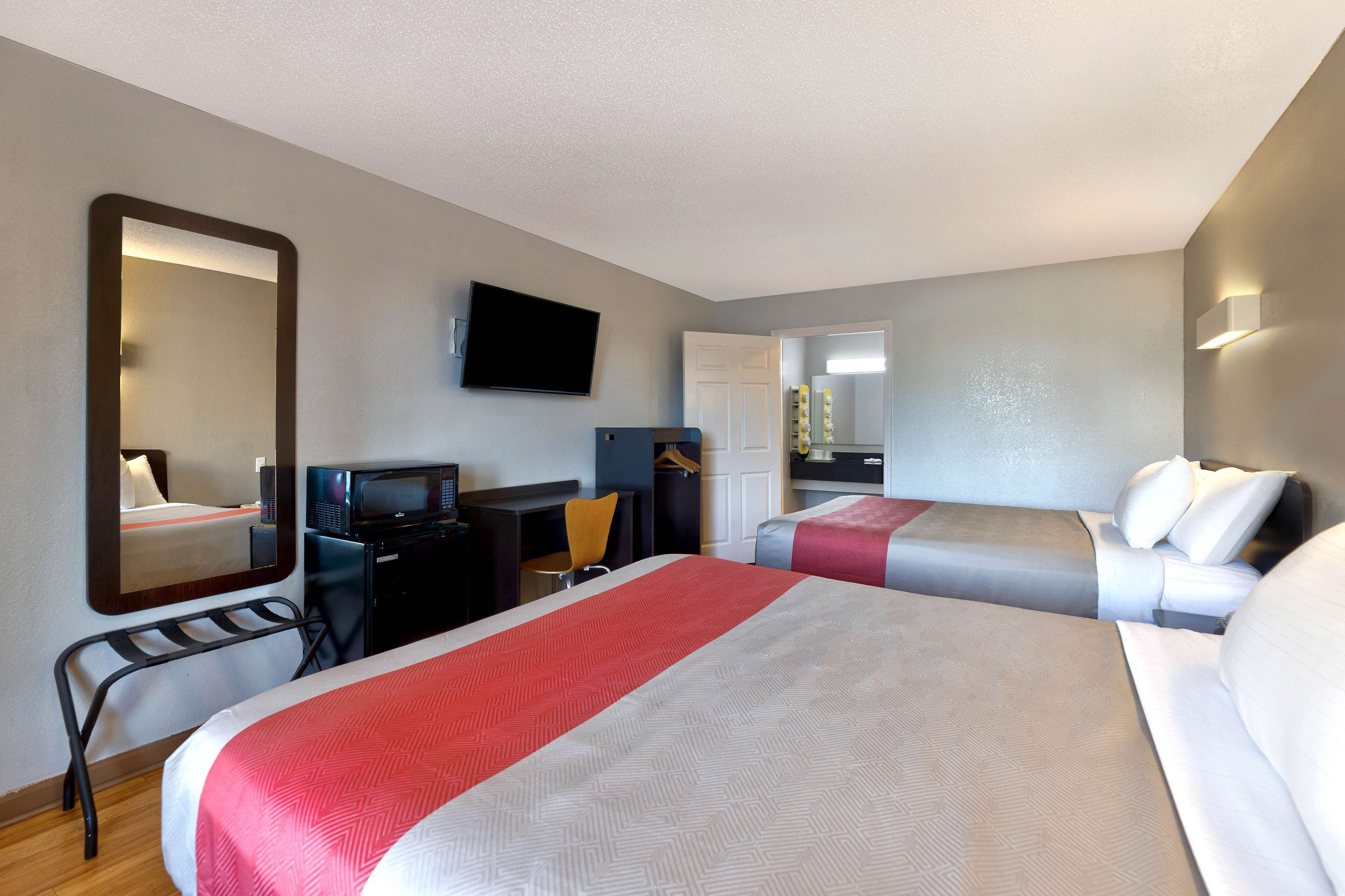 A hotel room with two beds, a desk, a chair, a TV, and a mirror.