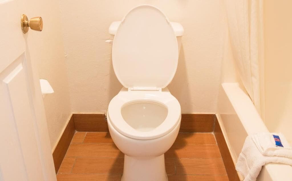 A small bathroom with a white toilet, wooden floor, and a towel hanging on the wall.