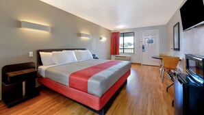 Une chambre d’hôtel avec un lit, un bureau, une télévision et une fenêtre avec des rideaux.
