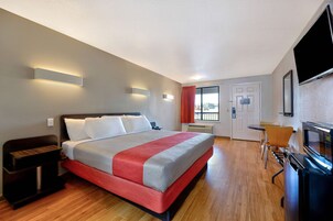 Una habitación de hotel con cama, escritorio, televisor y ventana con cortinas.