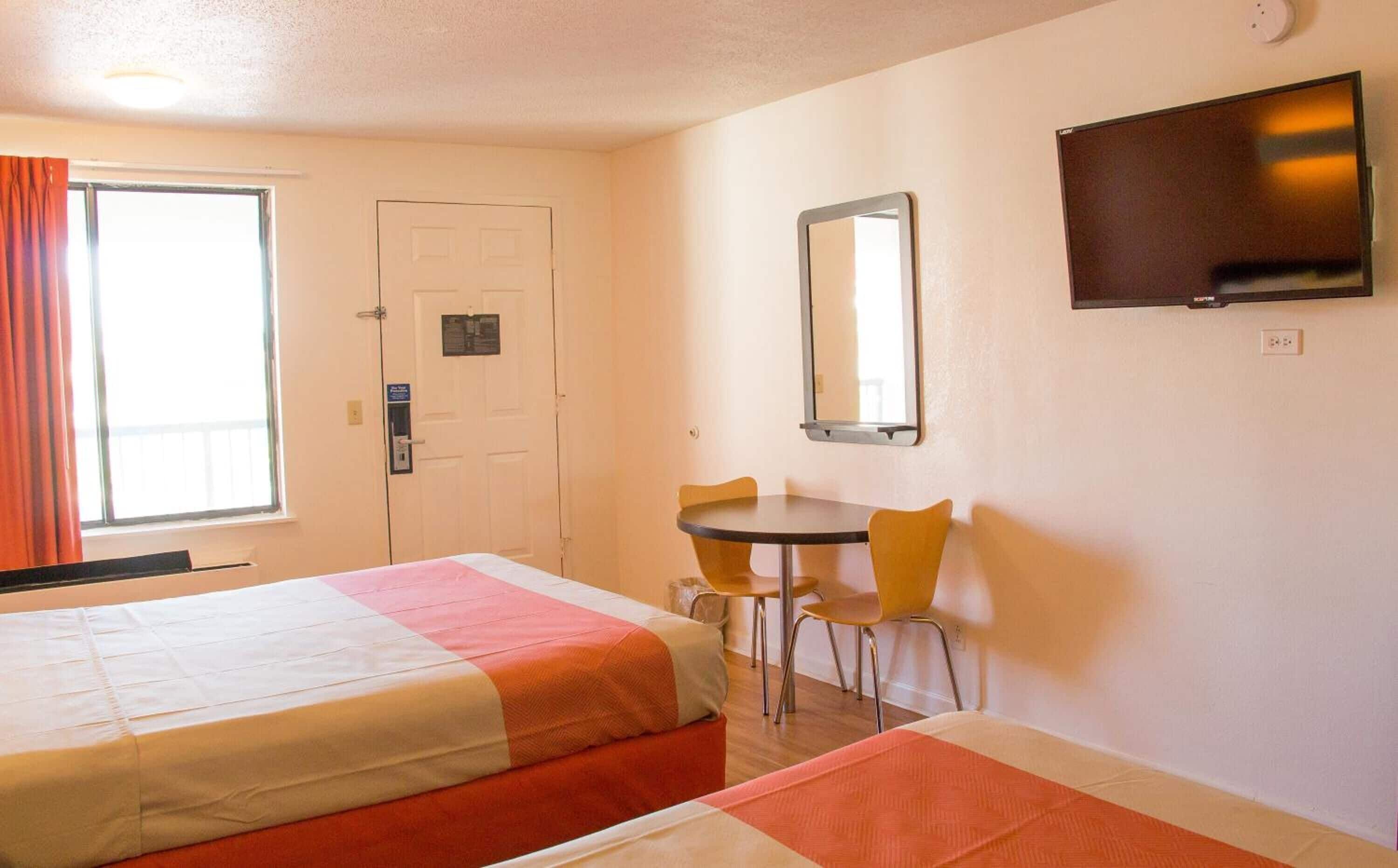 A hotel room with two beds, a desk, a chair, a television, and a door.