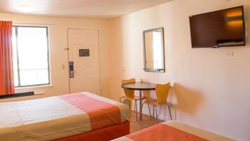 A hotel room with two beds, a desk, a chair, a television, and a door.