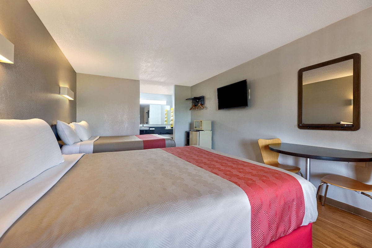 Een hotelkamer met twee bedden, een bureau, een stoel, een televisie en een spiegel.