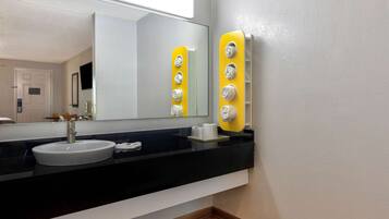 Een badkamer met een wit wastafel, een zwart aanrecht en een spiegel. Er zijn gele handdoekhouders en een witte beker op het aanrecht.