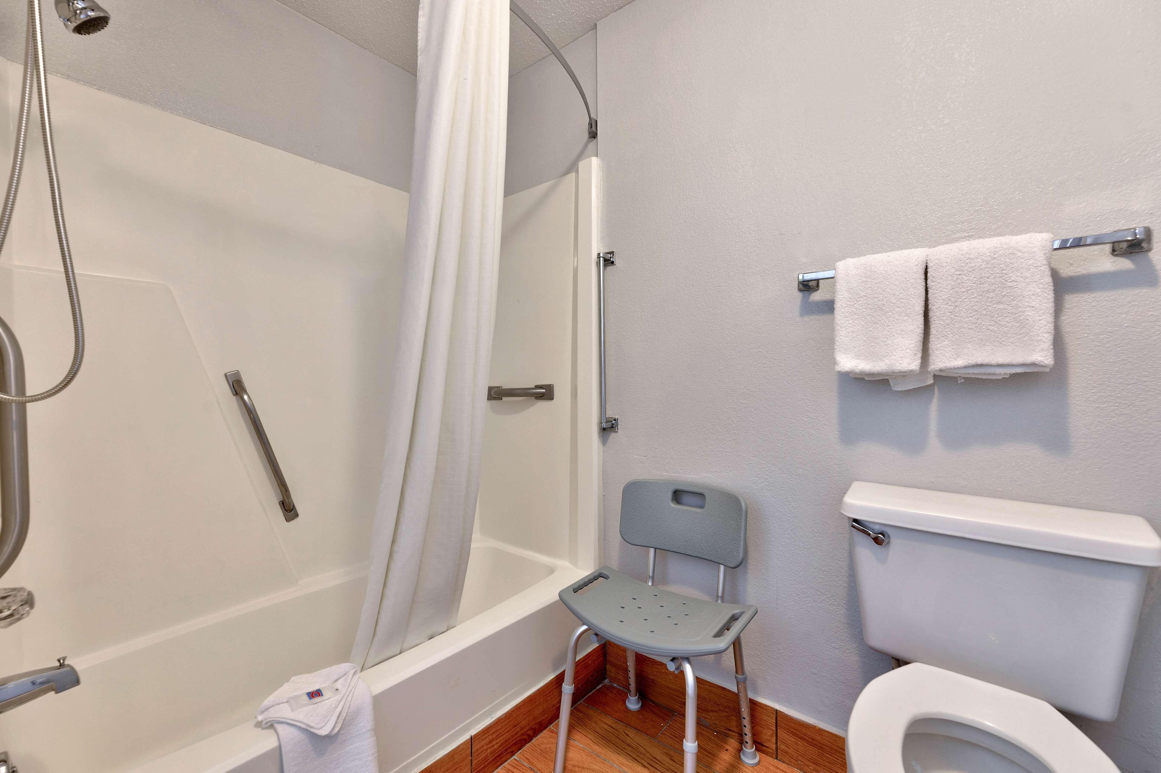 A bathroom with a shower, toilet, and a chair.