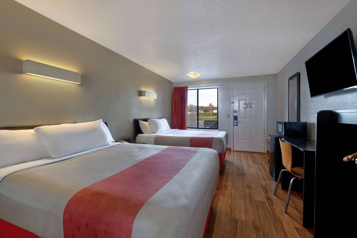 Een hotelkamer met twee bedden, een bureau met stoel, een televisie en een deur naar een balkon.