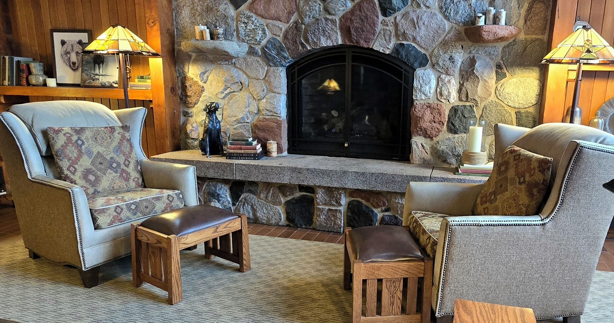 A cozy living room with a stone fireplace, leather armchairs, and a wooden coffee table.