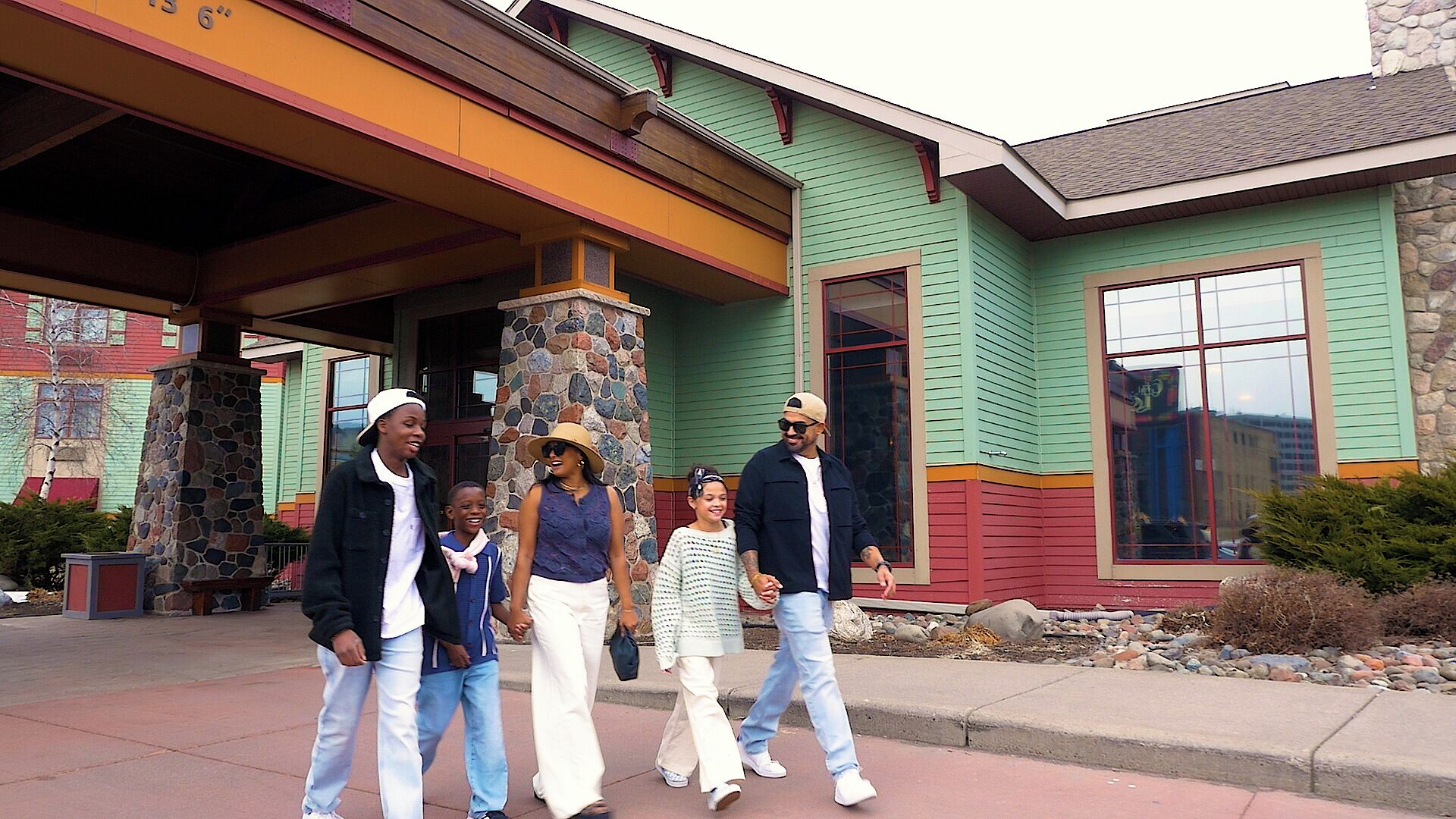 A family walking in front of a building with a stone pillar, a porch, and a large window.