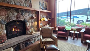 A stone fireplace with a fire, a leather chair, a sofa, and a view of a bus through large windows. - Canal Park Lodge (Duluth)
