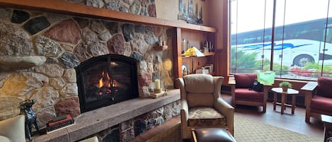 Una chimenea de piedra con fuego, un sillón de cuero, un sofá y una vista de un autobús a través de amplias ventanas.