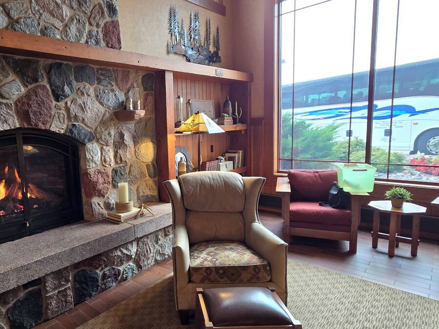A stone fireplace with a fire, a leather chair, a sofa, and a view of a bus through large windows.
