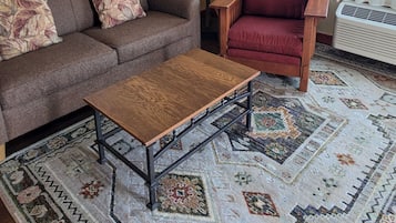 A living room with a sofa, armchair, coffee table, floor lamp, and patterned rug.