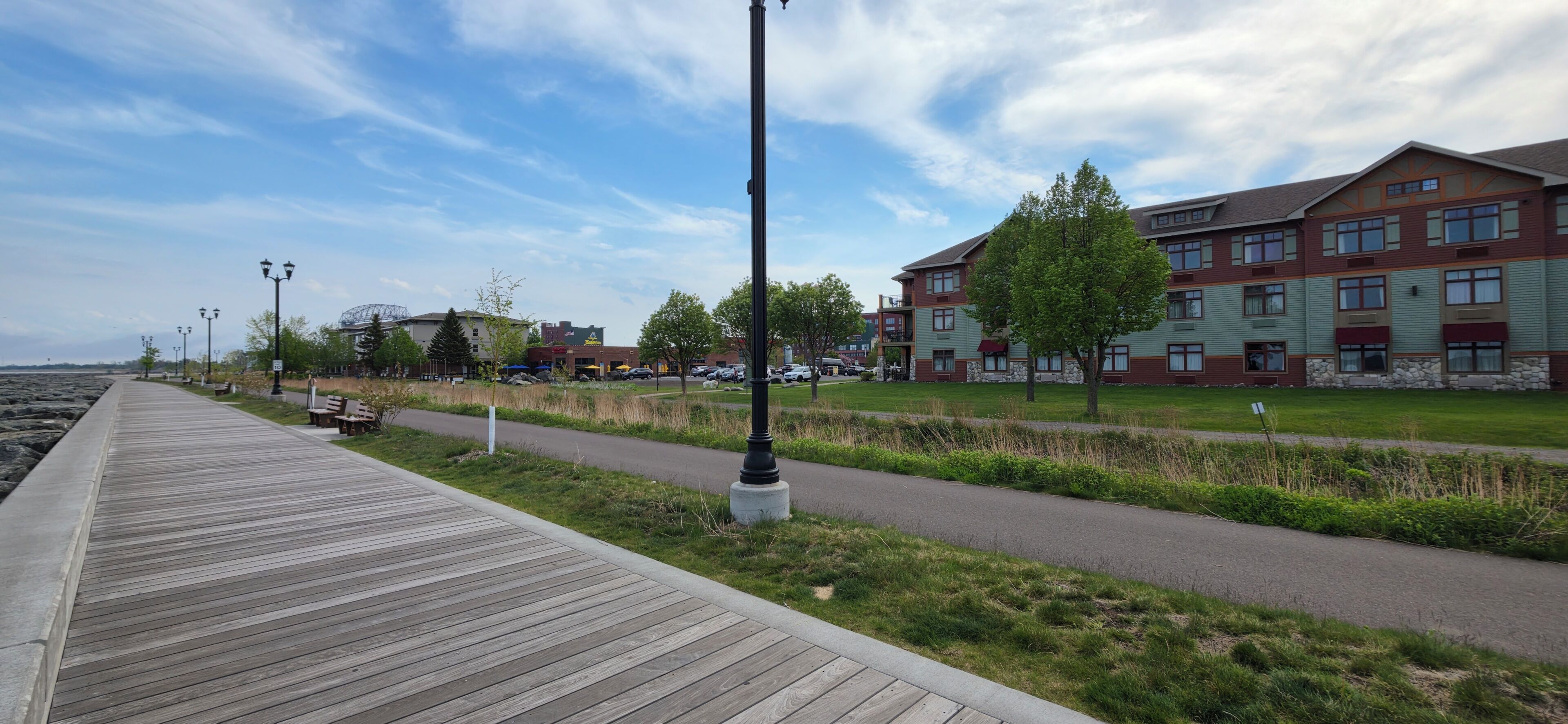 A wooden boardwalk, a paved path, and a multi-story building with a green and red facade.