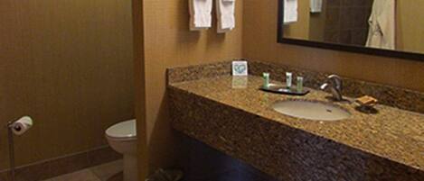 Une salle de bain avec un lavabo doté d’un plan de travail en granit, un miroir et deux serviettes blanches suspendues à un porte-serviettes.