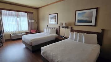 A hotel room with two beds, a desk, a chair, a lamp, and a picture on the wall.