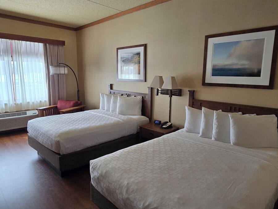 A hotel room with two beds, a desk, a chair, a lamp, and a picture on the wall.