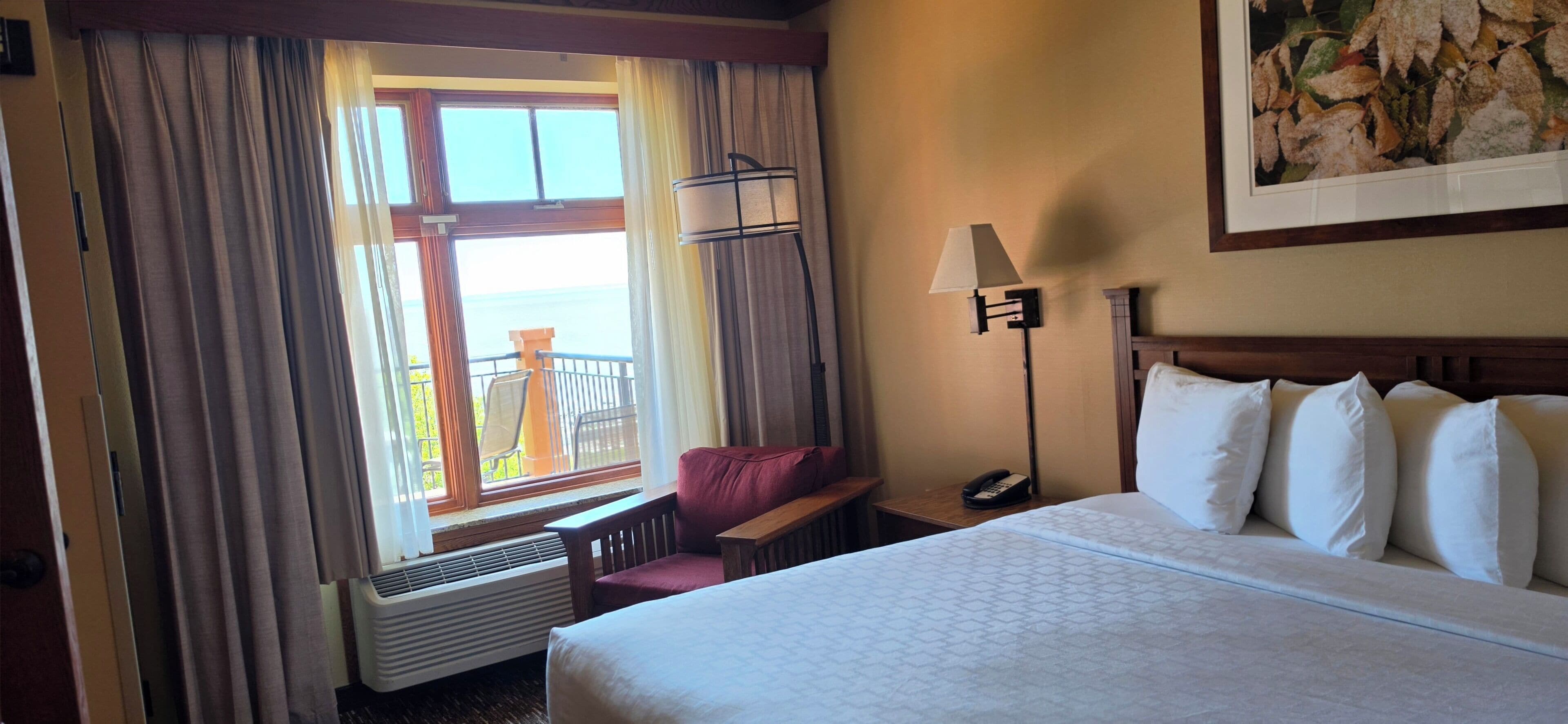 A hotel room with a bed, a chair, a nightstand with a lamp, a phone, and a window with curtains.
