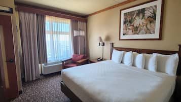 Quarto de hotel com uma cama grande, uma cadeira, uma escrivaninha, um abajur e um quadro na parede.