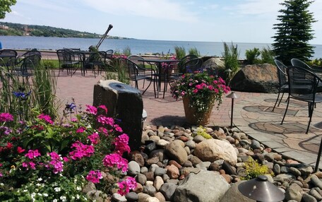 An outdoor seating area with tables and chairs, a rock garden with flowers, and a view of the water.