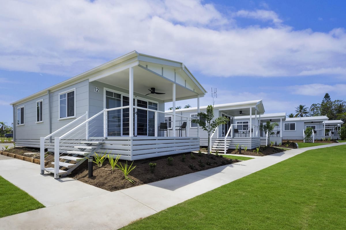 Una casa móvil moderna con un porche cubierto, una pequeña zona de estar al aire libre y un césped cuidado.