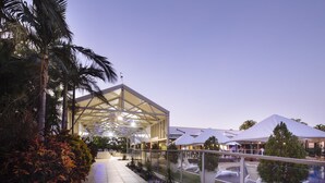 Un espacio exterior moderno con una estructura de vidrio, zonas de estar y una piscina.