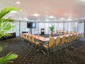 Une salle de conférence avec une longue table, des chaises, un écran de télévision et une plante.