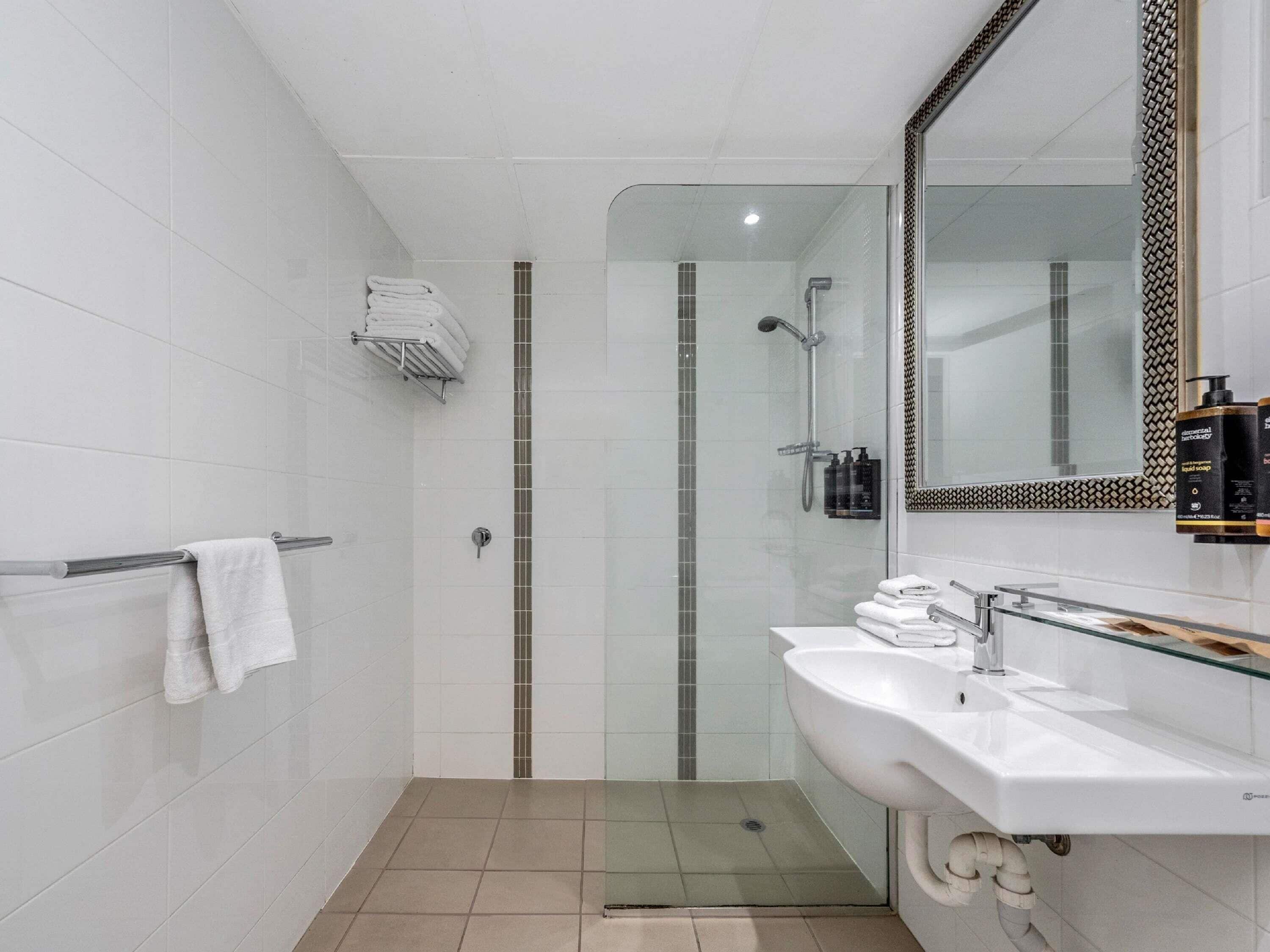A modern bathroom with a glass shower enclosure, a white sink with a glass countertop, and a large mirror with a decorative frame.