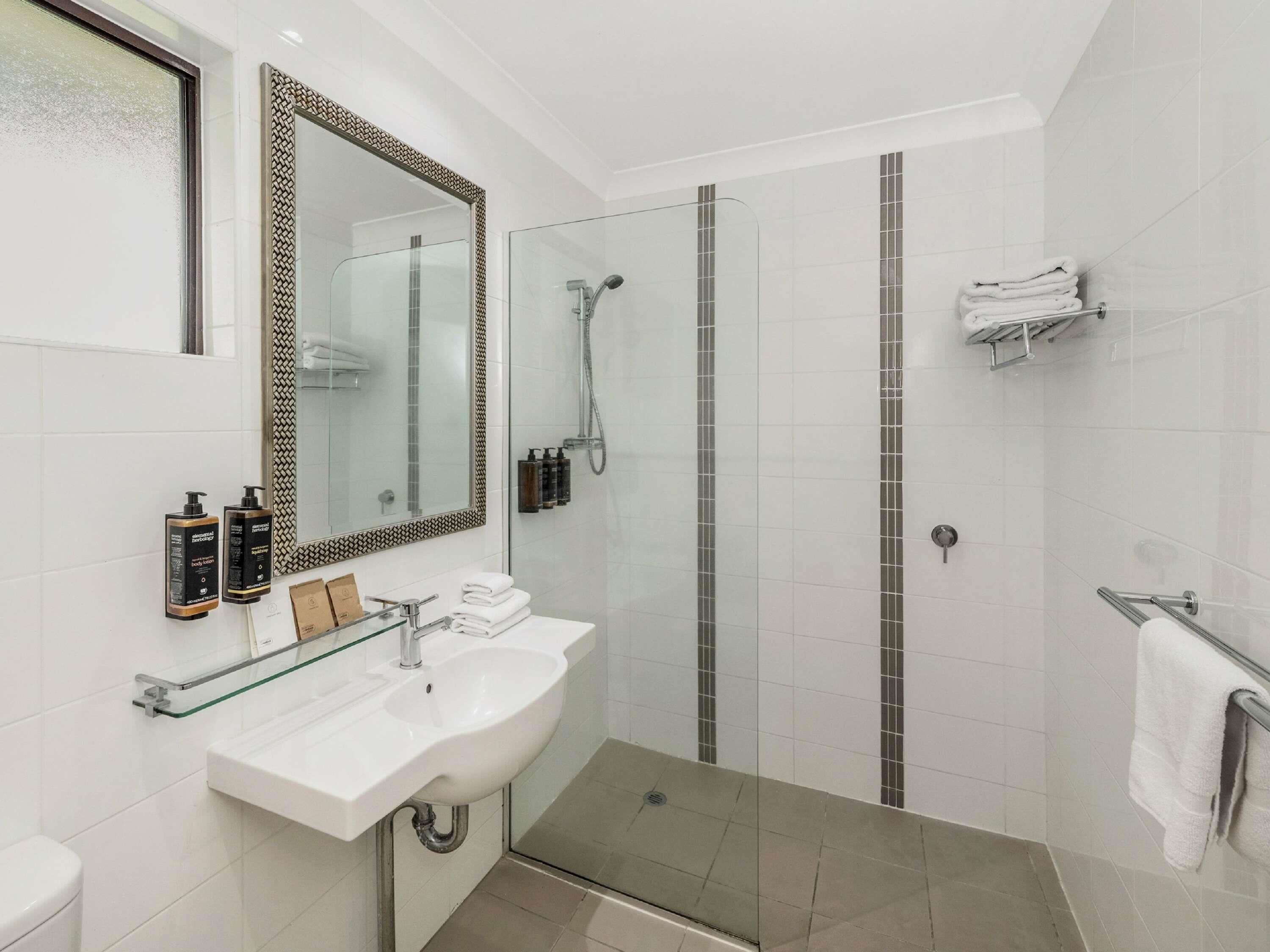 A modern bathroom with a glass shower enclosure, a white sink, and a large mirror.