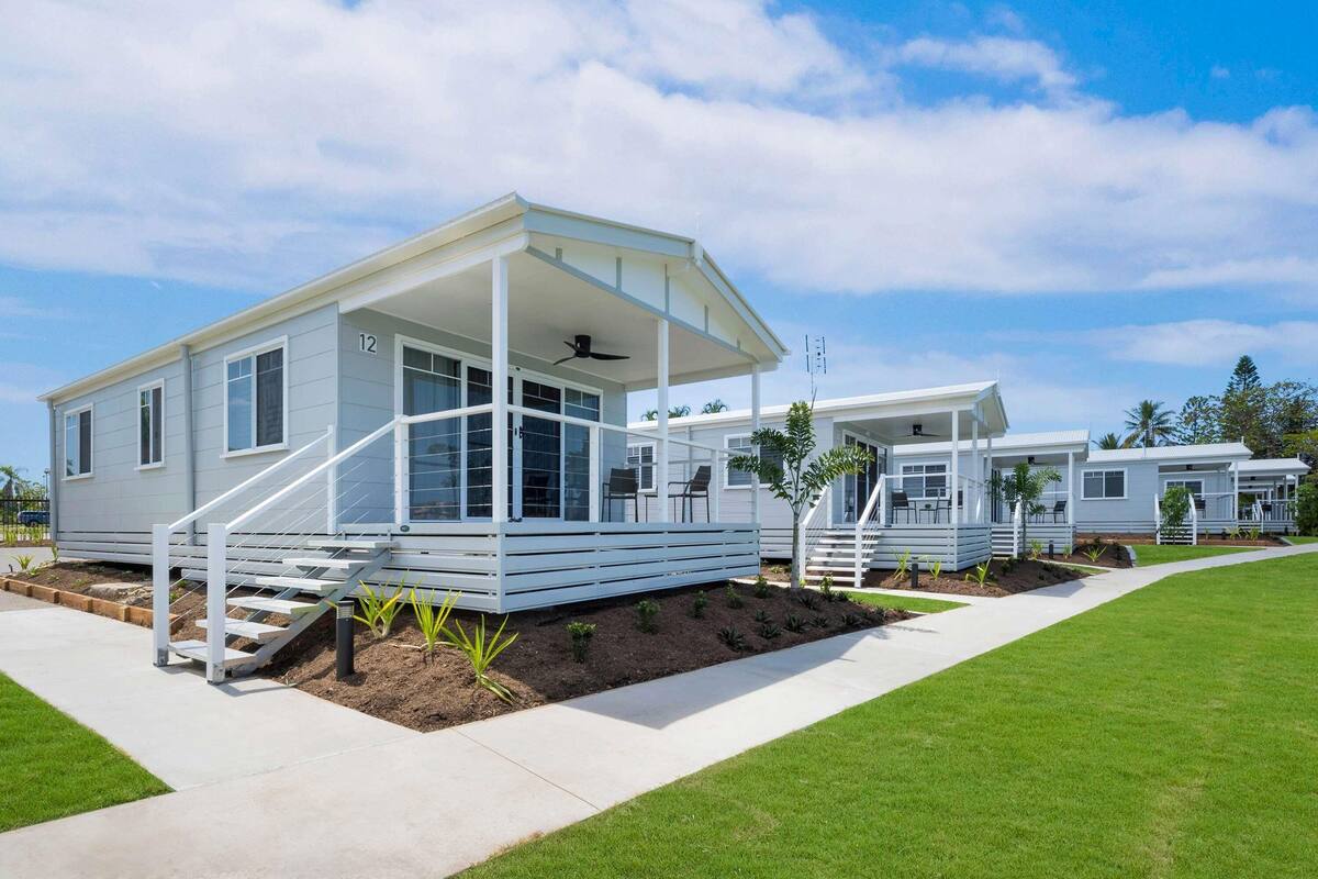 Une maison mobile moderne dotée d’un porche abrité, d’un petit espace extérieur aménagé pour s’asseoir et d’une pelouse bien entretenue.
