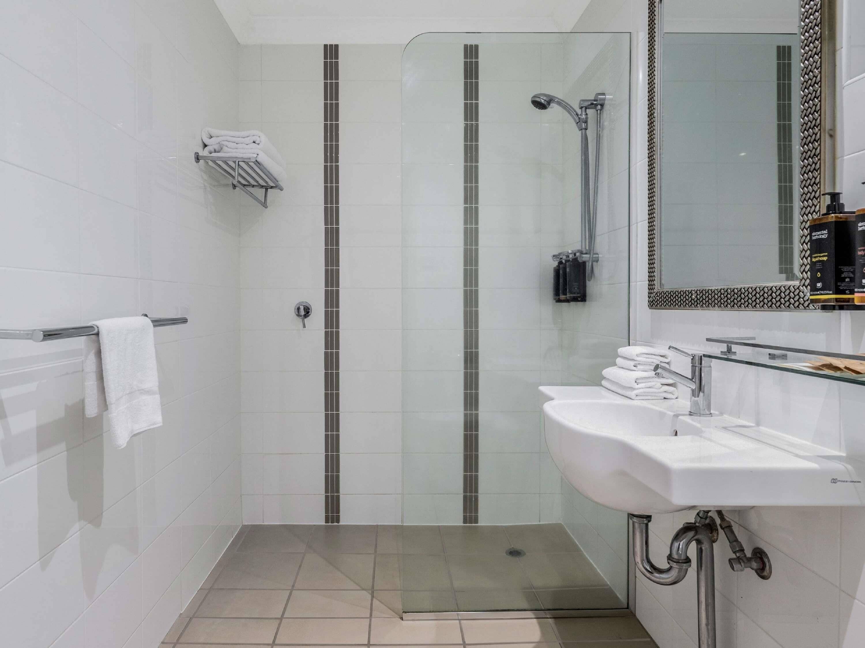 Une salle de bain moderne avec une douche à parois de verre, un lavabo blanc et un sol carrelé.