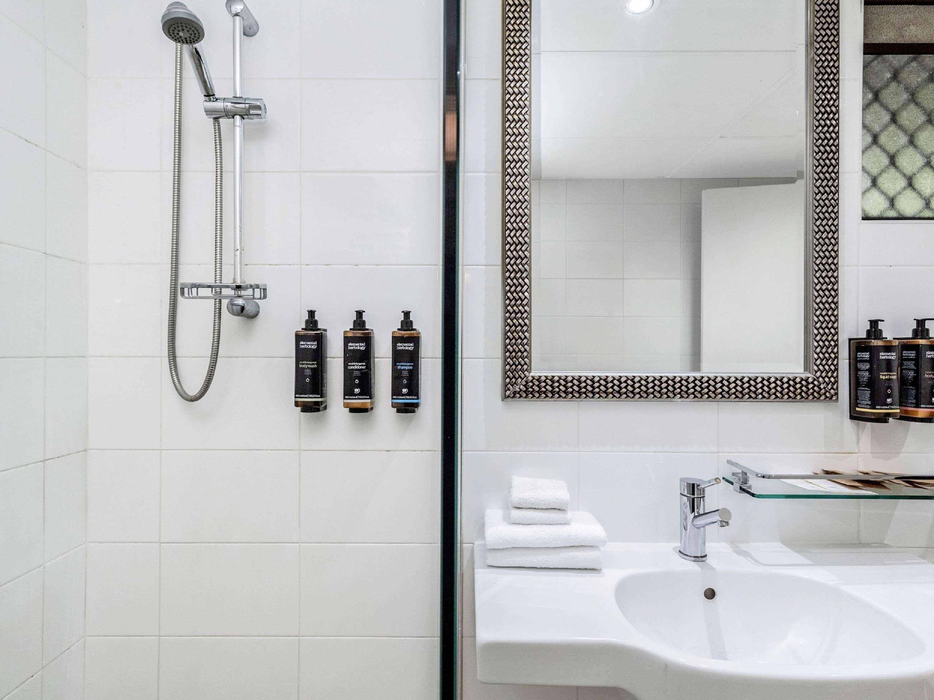 Une salle de bain équipée d’une douche, d’un lavabo et de trois flacons de produits de toilette.